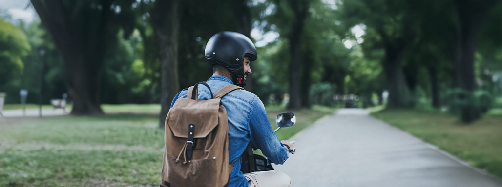 Ein Mann mit Rucksack färt mit einem Roller auf der Straße.
