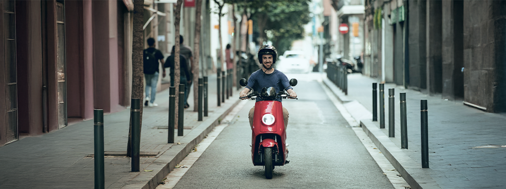 Ein Mann fährt mit einem roten Mofa auf einer Straße.