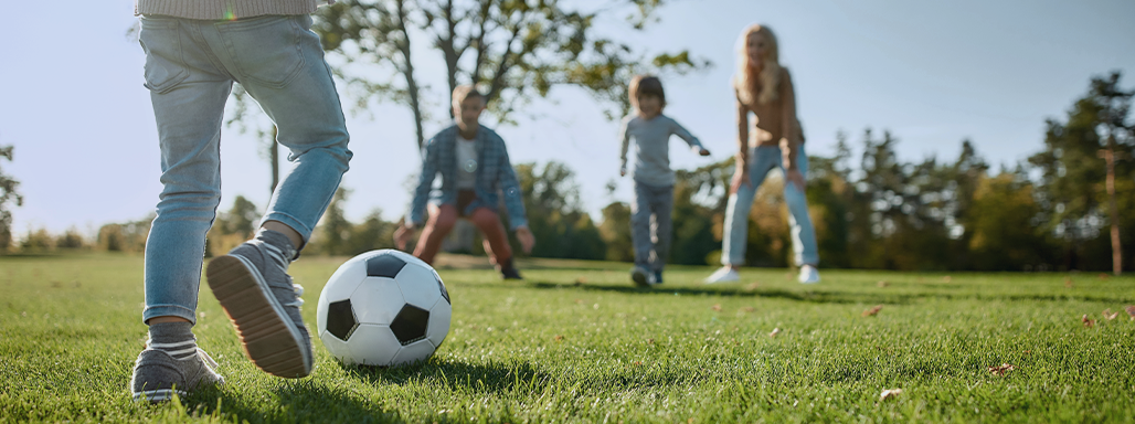 Ein kleines Kind spielt Fußball mit seiner Familie auf einer grünen Wiese.