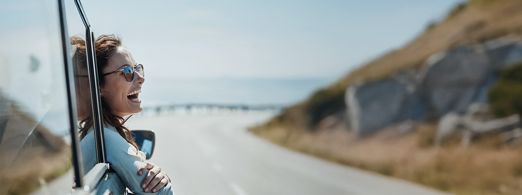 Frau lehnt sich lachend aus dem Beifahrerfenster eines fahrenden Autos.