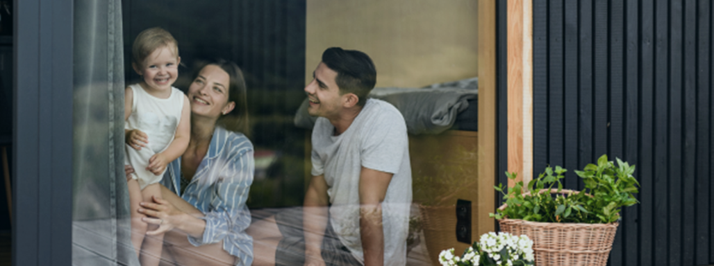 Junge Familie, bestehend aus Vater, Mutter und Kind, sitzen am Fenster und schauen glücklich raus.