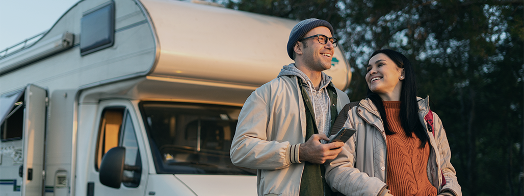 Ein junges Paar steht lächelnd vor einem Wohnmobil.