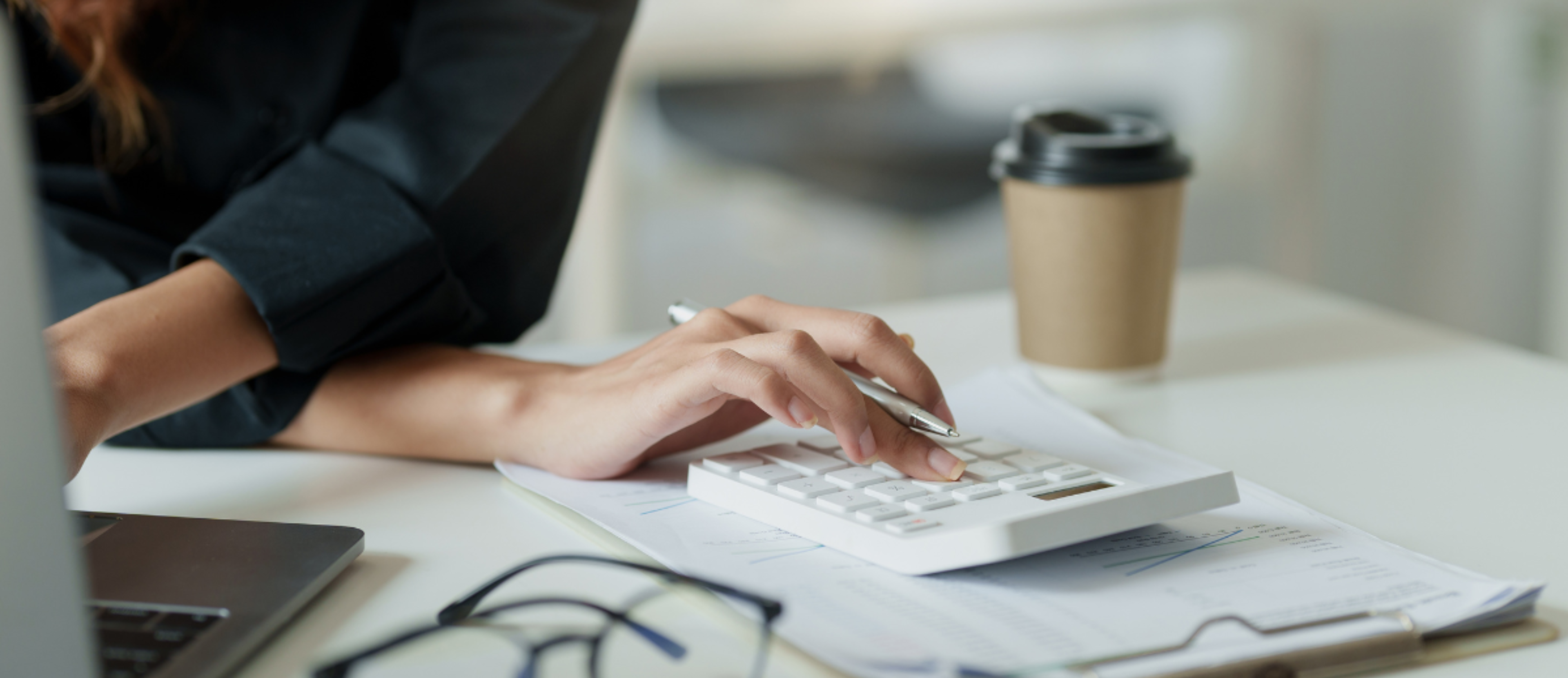 Frau mit Taschenrechner und Laptop am Schreibtisch