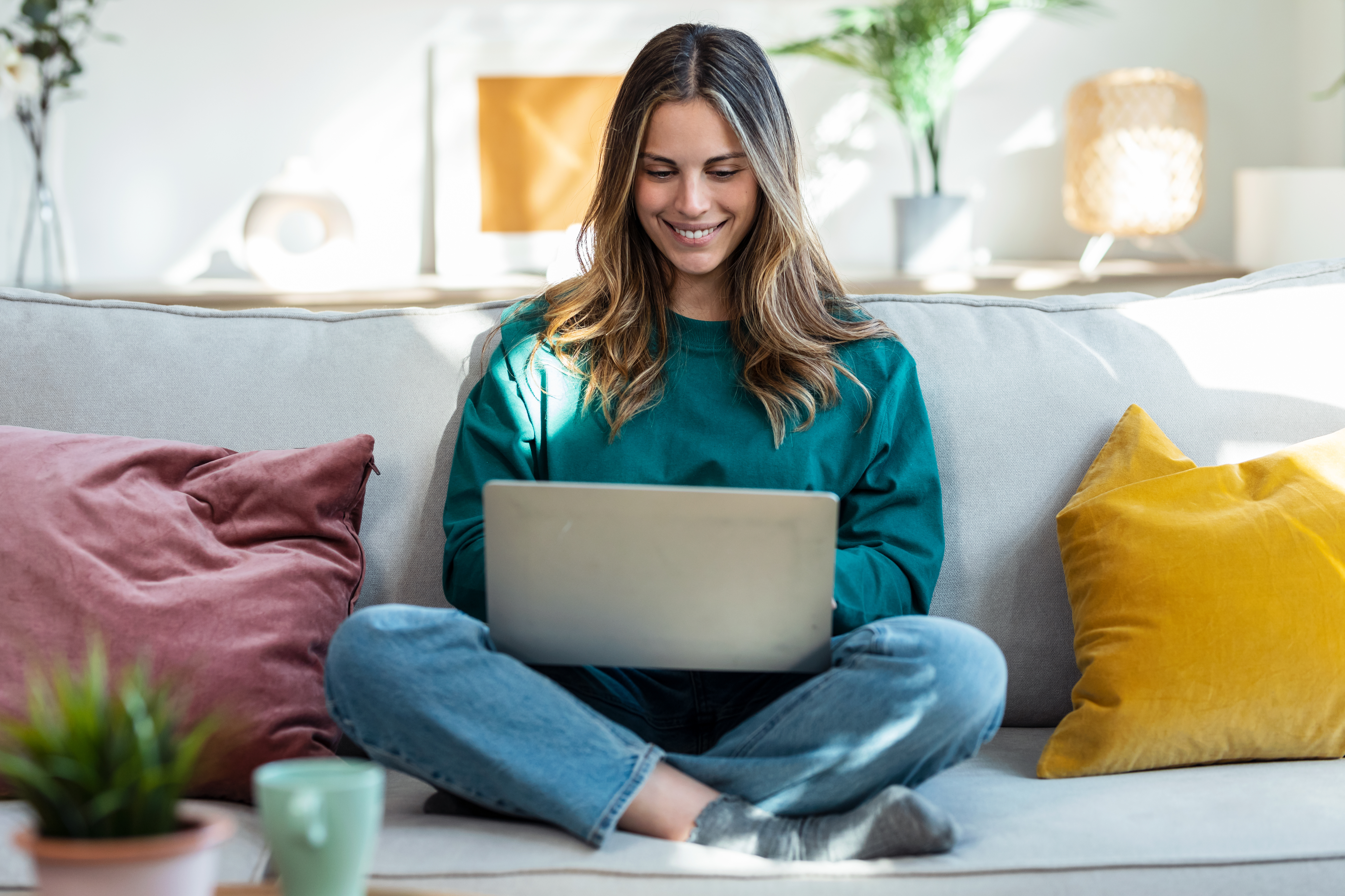 Junge Frau sitzt lächelnd an ihrem Laptop auf dem Sofa